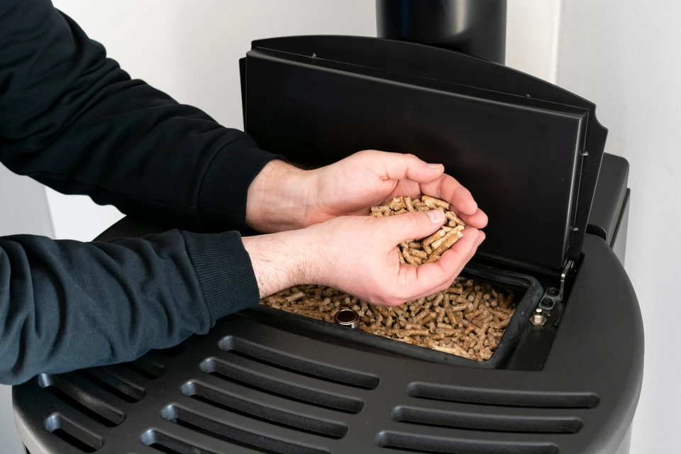 Une personne en pull noir manipule des granulés de bois, tenant une poignée au-dessus d'un réservoir de poêle à pellets ouvert