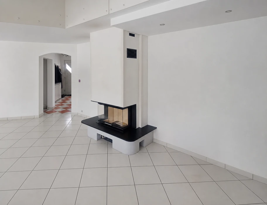 Salon vide avec cheminée contemporaine encastrée à foyer fermé vitré trois faces, habillage blanc avec tablette en granit noir, conduit de fumée apparent