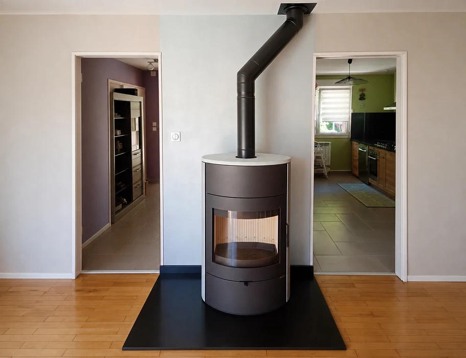 Poêle à bois design cylindrique, finition anthracite mat avec dessus blanc, vitré sur façade, posé sur dalle noire au sol en parquet
